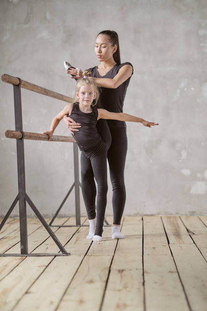happy woman and little girl study in classroom. teacher and teacher in the dance class. individual sessions. teacher carefully helps to stretch the muscles - Photo, Image