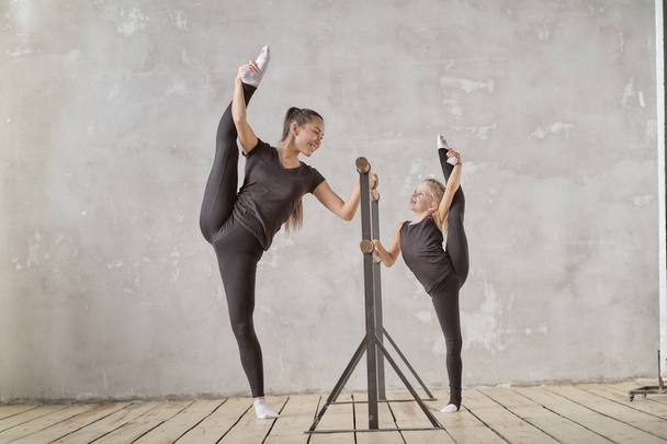 ευτυχισμένη γυναίκα και ένα μικρό κορίτσι σπουδάζουν στην τάξη. δάσκαλος και δασκάλα στο μάθημα χορού. μεμονωμένες συνεδρίες. Δάσκαλος βοηθά προσεκτικά να τεντώσει τους μυς - Φωτογραφία, εικόνα