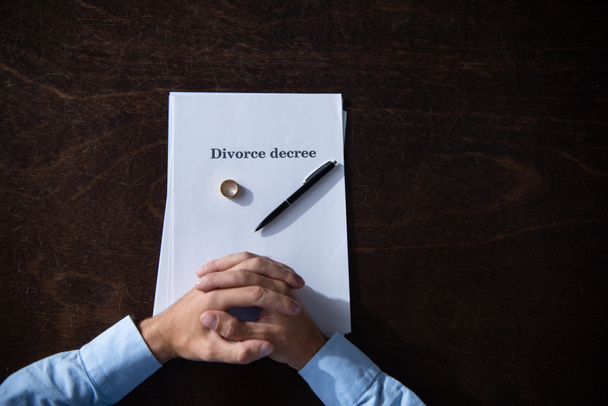 boşanma belgeleri ile sıkıştırılmış elleri ile masada oturan adam kısmi görünümü - Fotoğraf, Görsel