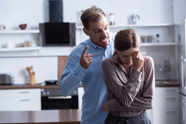 aggressive man in shirt screaming at crying wife during quarrel - Foto, afbeelding