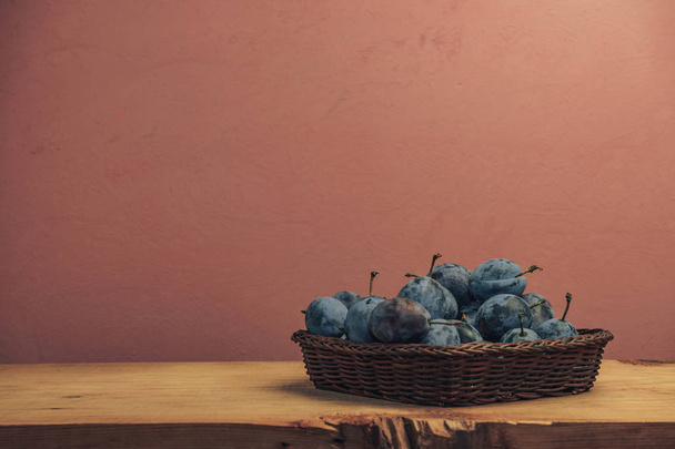 Hermosas ciruelas frescas en cesta sobre una mesa de madera marrón y fondo de pared rojo
. - Foto, imagen