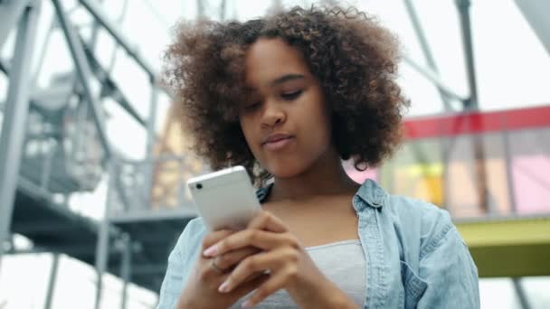 African American teenager is using modern smartphone outdoors in the street - Metraje, vídeo
