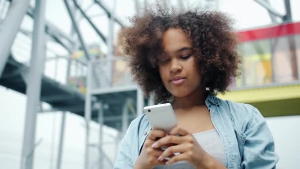 Happy African American girl looking at smartphone screen smiling outdoors - Materiał filmowy, wideo