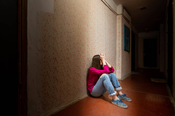 Mujer triste y desesperada se sienta en un pasillo oscuro
 - Foto, imagen