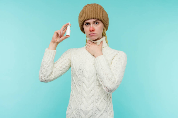 Chory młoda kobieta w szalik i kapelusz używać aerozol do nosa na białym tle - Zdjęcie, obraz