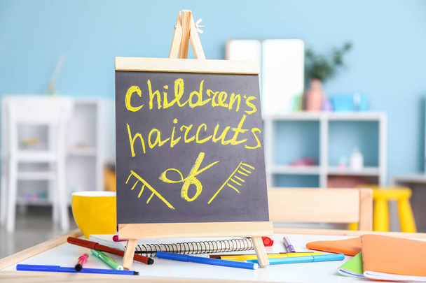 Chalkboard with written inscription CHILDREN'S HAIRCUTS in salon - Photo, Image
