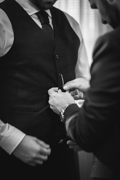 Vertical grayscale shot of a male buttoning his friend's jacket for the wedding - Fotografie, Obrázek