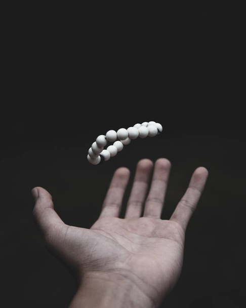 Shallow focus shot of a male's hand throwing white beads upwards on a dark background - Φωτογραφία, εικόνα