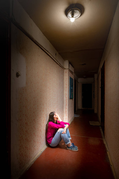 Traurige und verzweifelte Frau sitzt in einem dunklen Flur - Foto, Bild