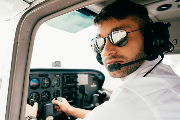пилот в солнцезащитных очках и гарнитуре смотрит в камеру в самолете
 - Фото, изображение