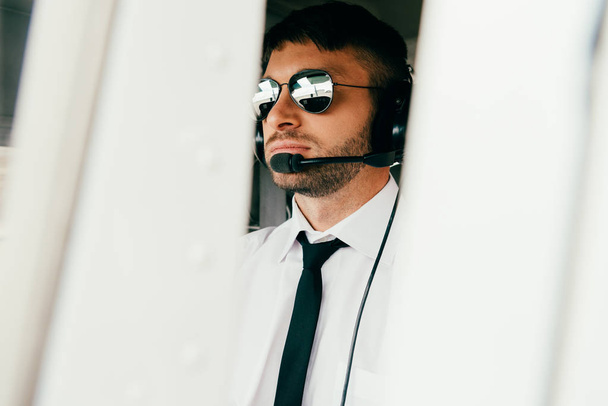 σοβαρός πιλότος σε γυαλιά ηλίου και ακουστικά κοιτάζοντας μακριά - Φωτογραφία, εικόνα
