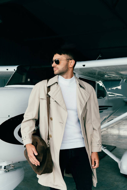 mietteliäs tyylikäs liikemies turkissa seisoo lähellä lentokonetta ja katselee poispäin
 - Valokuva, kuva