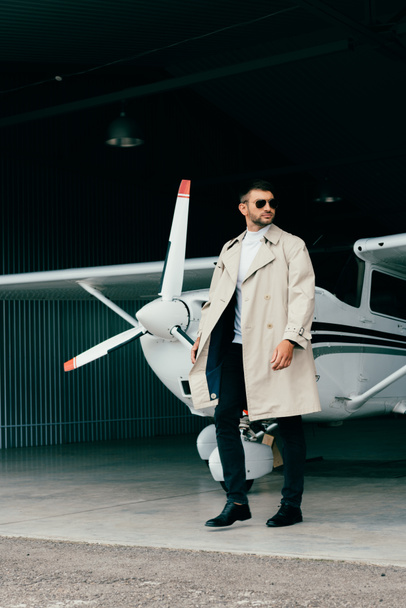 full length view of stylish businessman in coat standing near plane - Foto, immagini