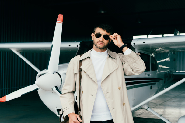 pensive stylish businessman in coat standing near plane - Fotoğraf, Görsel