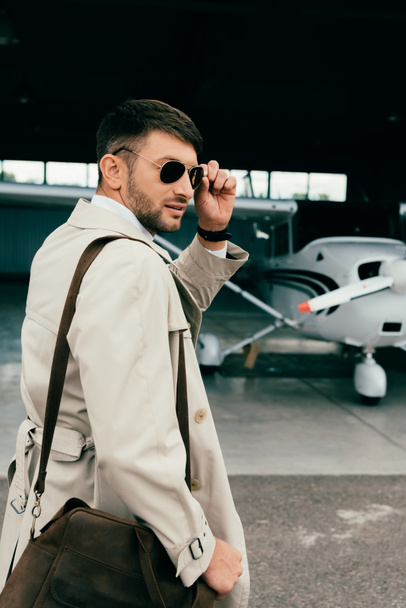 pensativo hombre de negocios con estilo en abrigo de pie cerca de avión
 - Foto, imagen
