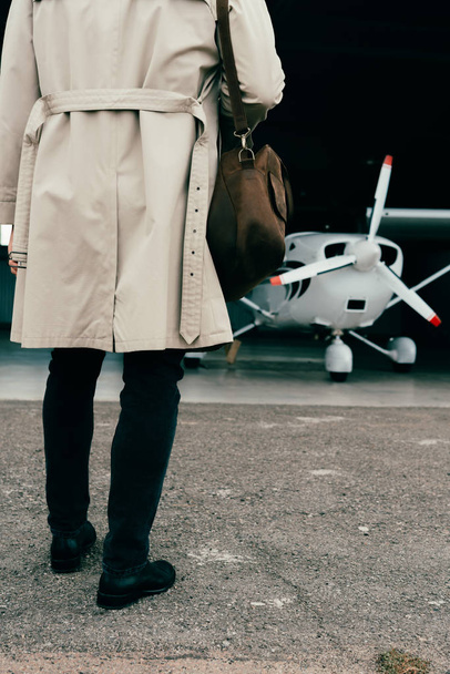partial view of stylish businessman in coat standing near plane - Foto, afbeelding