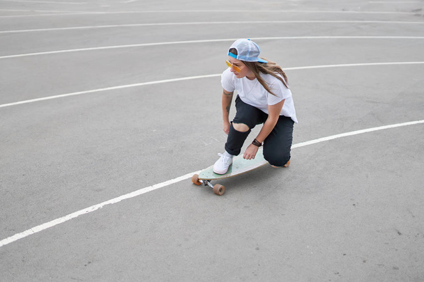 Photo on side of brunette woman in baseball cap riding skateboard outdoors - Foto, afbeelding