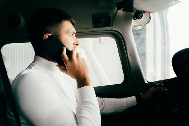 side view of pilot talking on smartphone in plane - Fotó, kép