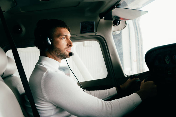 fokussierter gutaussehender bärtiger Pilot im Headset im Flugzeug - Foto, Bild