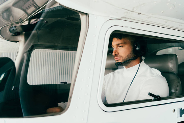 skoncentrowany Brodaty pilot w słuchawkach siedzi w samolocie - Zdjęcie, obraz