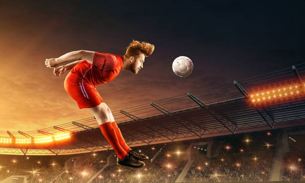 Ο ποδοσφαιριστής κλωτσάει την μπάλα με το κεφάλι. Γήπεδο ποδοσφαίρου με θεατές και νυχτερινό δραματικό ουρανό - Φωτογραφία, εικόνα