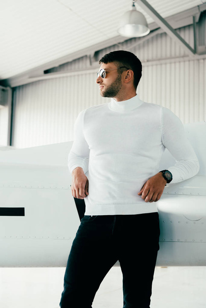 pensive man in sunglasses standing near plane and looking away - 写真・画像