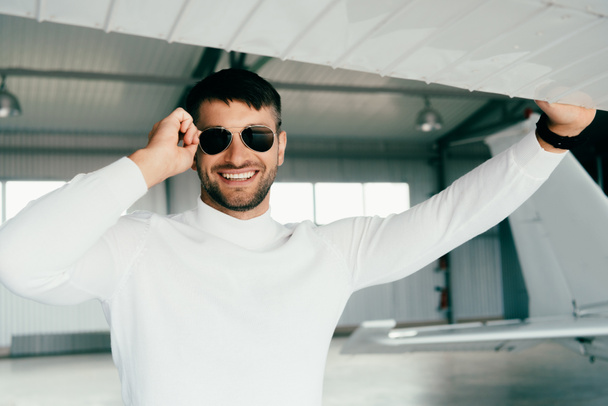 front view of smiling bearded man in sunglasses standing near plane - Fotografie, Obrázek