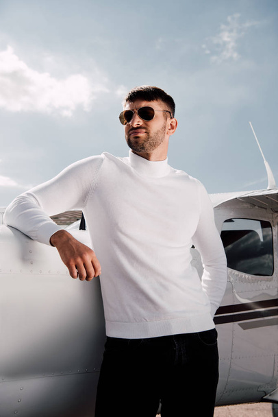 low angle view of bearded man in sunglasses standing near plane in sunny day - Valokuva, kuva