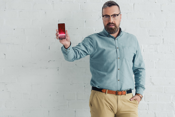 handsome businessman with hand in pocket holding smartphone with trading courses website  - Foto, imagen