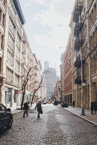 Vertical shot of people crossing a road between brown and white buildings - Foto, imagen