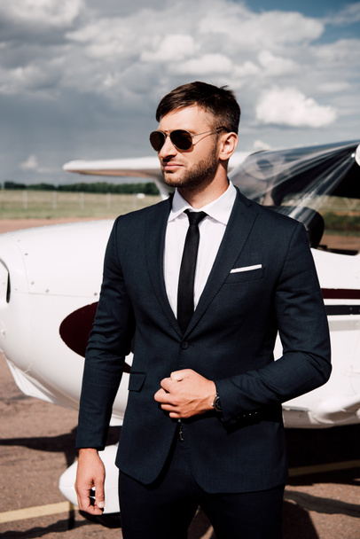 pensive businessman in formal wear standing near plane in sunny day - 写真・画像