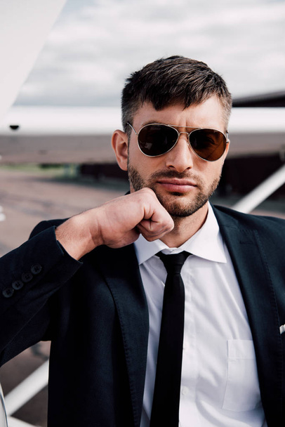 pensive businessman in formal wear standing near plane in sunny day - Fotografie, Obrázek