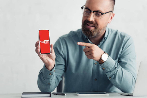 KYIV, UKRAINE - AUGUST 27, 2019: handsome businessman in shirt pointing with finger at smartphone with youtube logo - 写真・画像