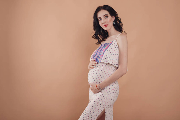 Donna incinta che tocca la pancia su sfondo beige
. - Foto, immagini