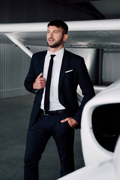 homem de negócios confiante no desgaste formal de pé com a mão no bolso perto do avião
 - Foto, Imagem