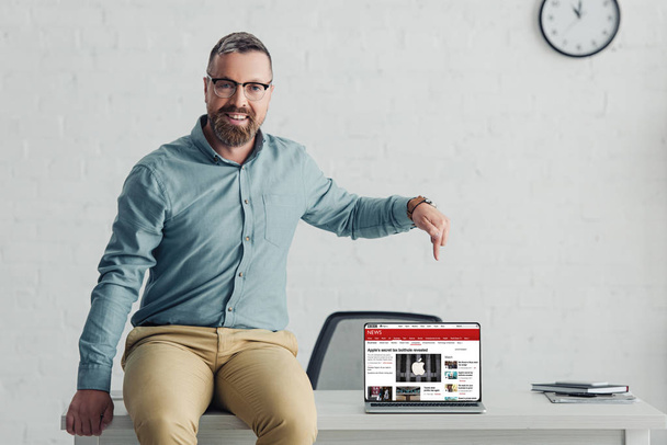 KYIV, UKRAINE - AUGUST 27, 2019: handsome businessman in shirt pointing with finger at laptop with bbs website - 写真・画像