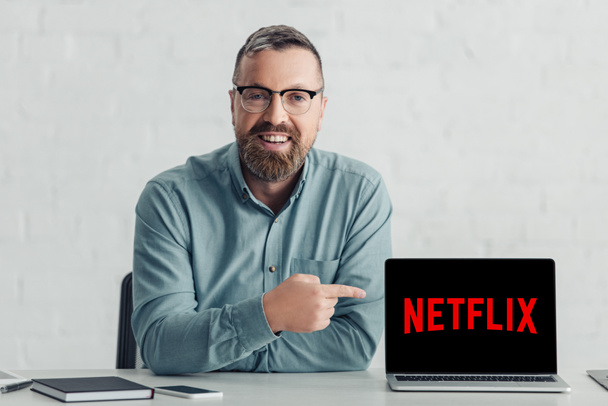 KYIV, UCRANIA - 27 de agosto de 2019: hombre de negocios guapo con camisa que señala con el dedo al ordenador portátil con el logotipo de netflix
 - Foto, Imagen