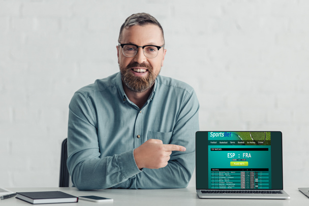 hombre de negocios guapo en camisa que apunta con el dedo a la computadora portátil con el sitio web de apuestas deportivas
  - Foto, imagen