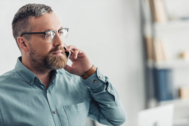 handsome businessman in shirt and glasses talking on smartphone in office  - Foto, Imagen