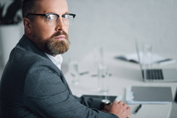 handsome businessman in formal wear and glasses looking at camera in office  - Photo, Image