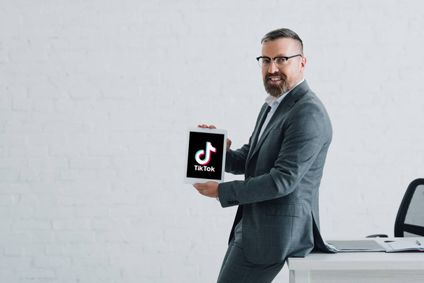 KYIV, UKRAINE - AUGUST 27, 2019: handsome businessman in formal wear holding digital tablet with tik tok logo - Foto, immagini