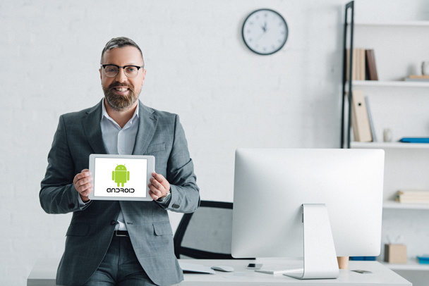 KYIV, UKRAINE - AUGUST 27, 2019: handsome businessman in formal wear holding digital tablet with android logo - 写真・画像