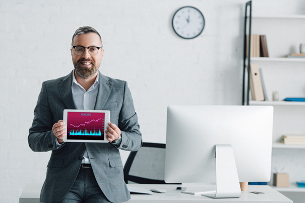 handsome businessman in formal wear holding digital tablet with graphs on screen - Zdjęcie, obraz
