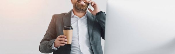 plano panorámico de hombre de negocios en ropa formal hablando en el teléfono inteligente y sosteniendo la taza de papel
 - Foto, imagen