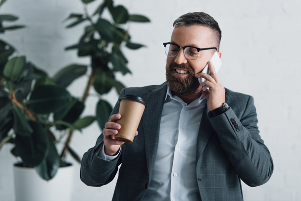 komea liikemies virallisessa kulumista puhuminen älypuhelimeen ja pitämällä paperimuki
 - Valokuva, kuva