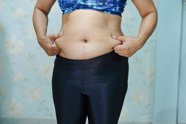 Υπερβολική ασιατική γυναίκα δείχνουν λίπος κοιλιά στο γραφείο. - Φωτογραφία, εικόνα
