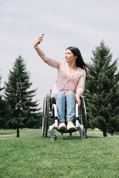 attractive disabled woman taking selfie on smartphone while walking in park - Fotó, kép