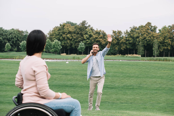 happy man talking on smartphone and waving hand to disabled girlfriend - 写真・画像