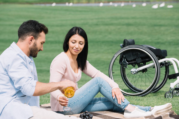 komea mies kaatamalla valkoviiniä lasiin, kun lepää puistossa vammaisen tyttöystävän kanssa
 - Valokuva, kuva