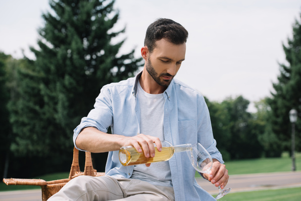 schöner Mann schenkt Weißwein in Glas im Park ein - Foto, Bild